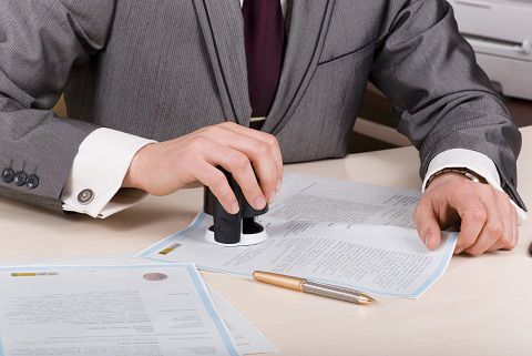 A person at a desk using a stamp or corporate seal on documents